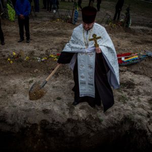 A priest is throwing dust at the grave of unknown Ukrainian soldier during mass burial ceremony in Dnipropetrovsk